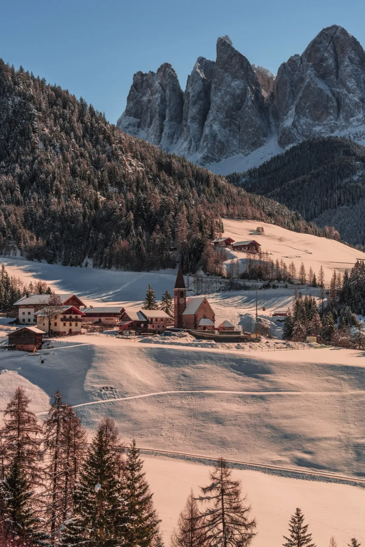 Val di Funes church and village under snow, the Odle peaks behind