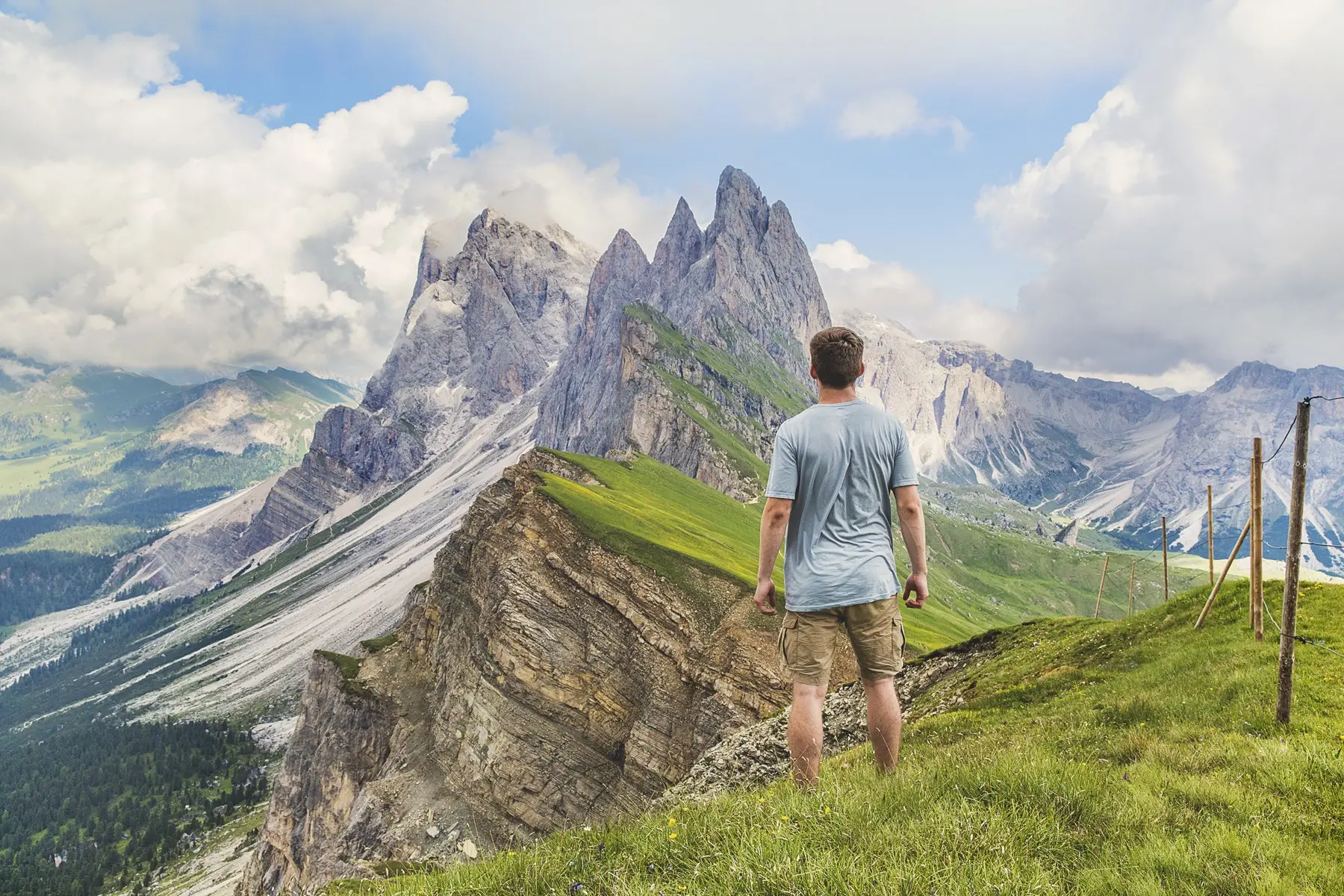 A walker on green pasture looking at the jagged Seceda ridge